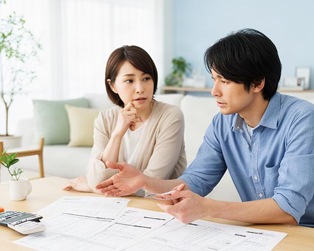 栗東市の明るいリビングで共働き夫婦が家計表を見ながら相談する様子